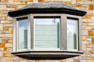 Bay window with three glass panels extending outward from a stone house facade.