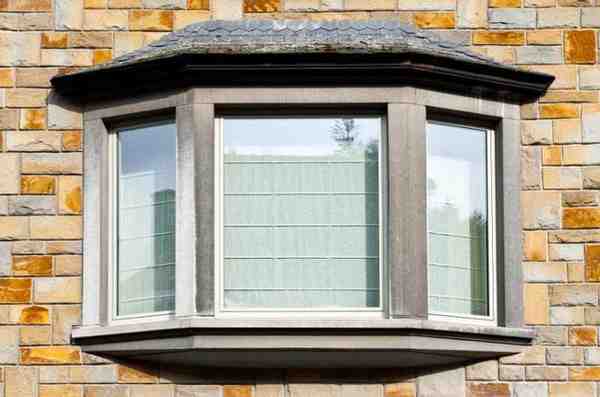 Bay window with three glass panels extending outward from a stone house facade.